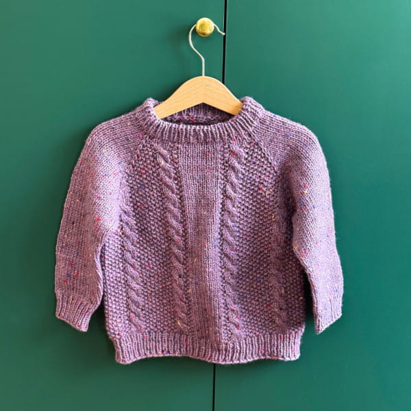 A cable sweater on a hanger